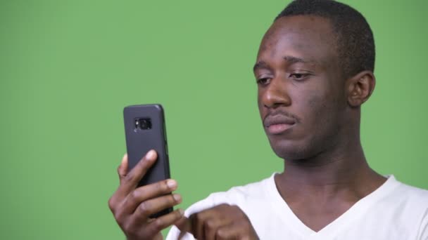 हिरव्या पार्श्वभूमी विरुद्ध फोन वापरून तरुण आफ्रिकन माणूस — स्टॉक व्हिडिओ