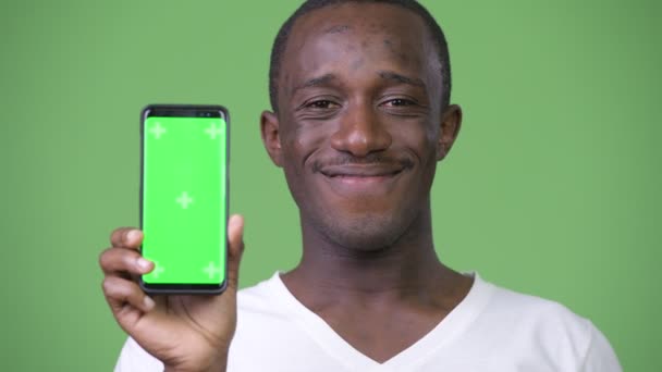 Молодой счастливый африканский мужчина улыбается, показывая телефон в камеру — стоковое видео
