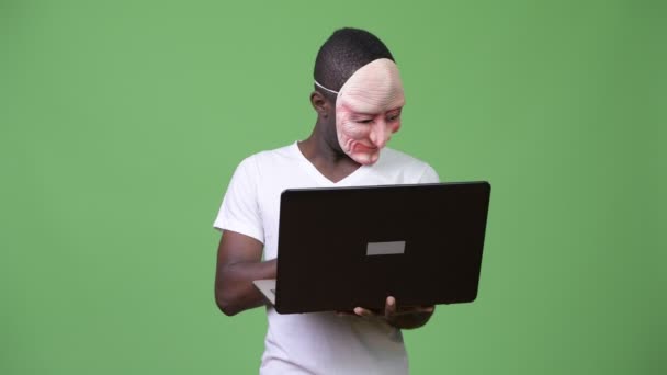 Junger afrikanischer Mann trägt Maske, während er Laptop benutzt — Stockvideo