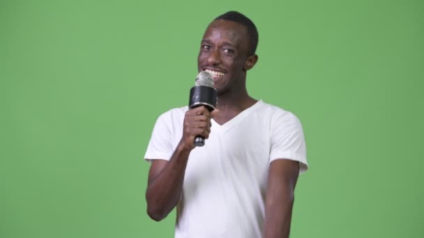 Молодой счастливый африканский мужчина улыбается, разговаривая по микрофону — стоковое видео