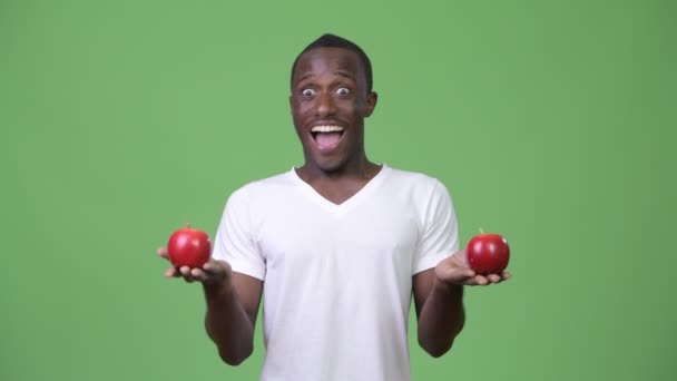 Jeune homme africain heureux souriant avec des pommes rouges — Video