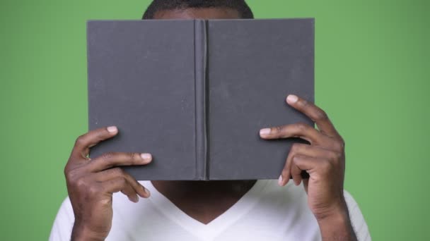 Unga afrikanska manbeläggning ansikte med bok — Stockvideo