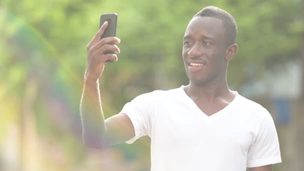 Šťastný afrického mladíka s úsměvem při používání telefonu v ulicích venku — Stock video