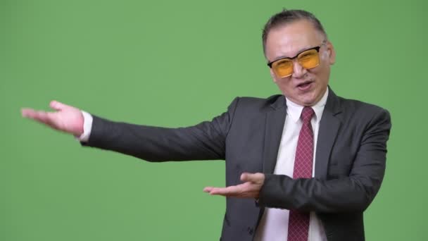 Mature Japanese businessman wearing sunglasses against green background — Stock Video