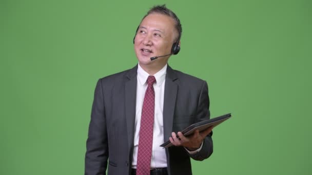 Зрілі японський бізнесмен працює як представник Центру дзвінок на зеленому тлі — стокове відео