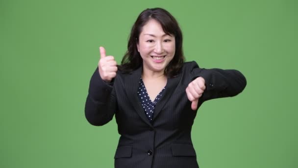 Mature confused Asian businesswoman giving thumbs up and thumbs down — Stock Video