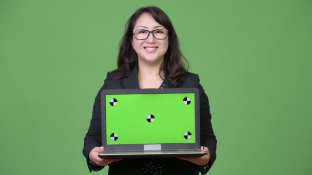 Ältere schöne asiatische Geschäftsfrau zeigt Laptop vor grünem Hintergrund — Stockvideo