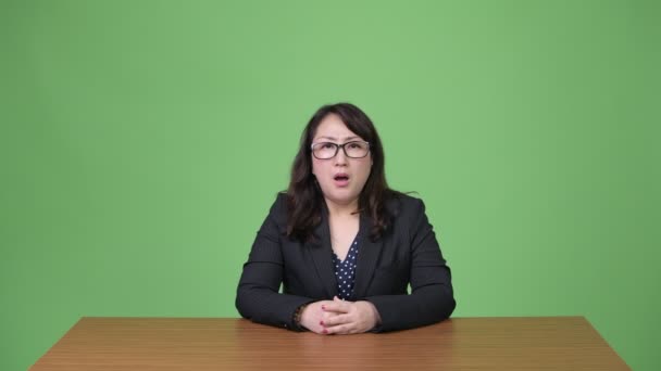 Mature beautiful Asian businesswoman having headache while sitting behind desk — Stock Video