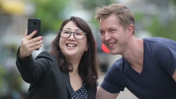 Reife asiatische Geschäftsfrau und junge skandinavische Mann mit Telefon zusammen in den Straßen im Freien — Stockvideo