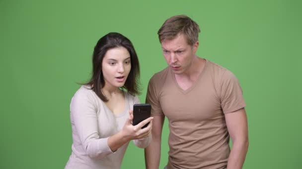 Νεαρό ζευγάρι ευτυχισμένο χρήση τηλεφώνου, ενώ ψάχνει ενθουσιασμένος μαζί — Αρχείο Βίντεο