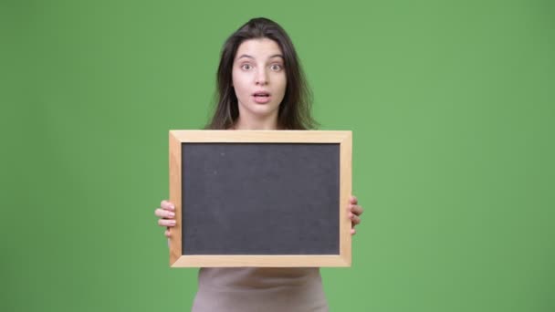 Young beautiful woman looking surprised while holding blackboard — Stock Video
