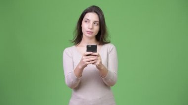 Telefon kullanarak ve yeşil arka planı düşünme genç güzel kadın