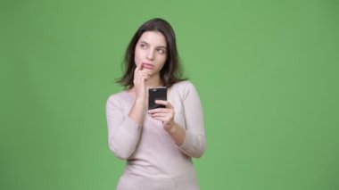Telefon kullanarak ve yeşil arka planı düşünme genç mutlu güzel kadın