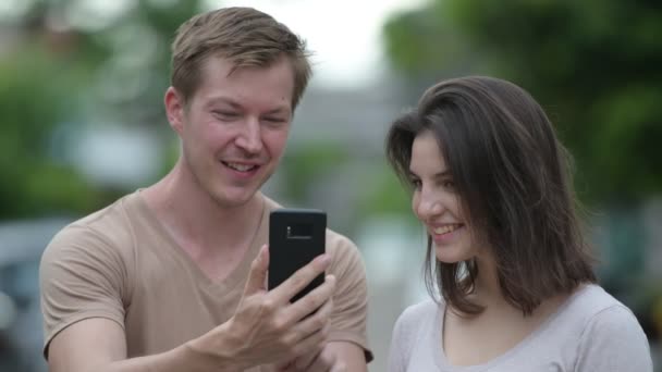 Jeune couple heureux utilisant le téléphone ensemble dans les rues à l'extérieur — Video