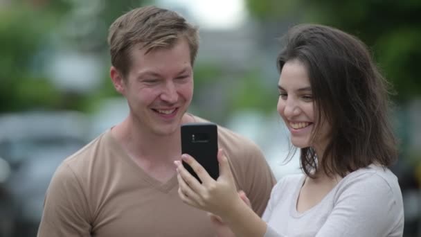 Joven pareja feliz usando el teléfono juntos en las calles al aire libre — Vídeo de stock