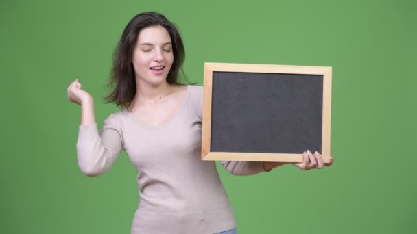 Junge glückliche schöne Frau gibt Daumen nach oben, während sie die Tafel hält — Stockvideo