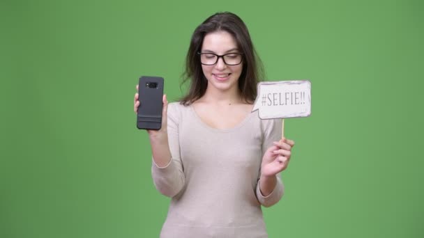 Joven feliz hermosa mujer sosteniendo teléfono y selfie papel signo — Vídeo de stock