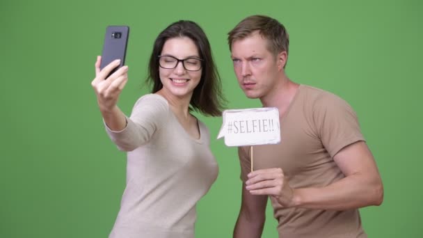 Happy νεαρό ζευγάρι λαμβάνοντας αυτοπορτρέτα μαζί ενάντια σε πράσινο φόντο — Αρχείο Βίντεο