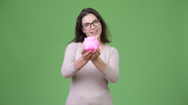 Mooie jongedame, houden piggy bank tegen een groene achtergrond — Stockvideo