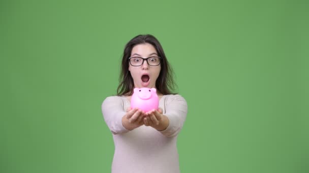 Junge schöne Frau hält Sparschwein vor grünem Hintergrund — Stockvideo
