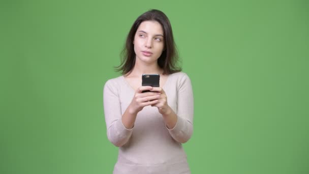 Joven hermosa mujer usando el teléfono y pensando en fondo verde — Vídeos de Stock