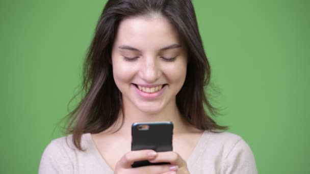 Jovem mulher bonita feliz sorrindo ao usar o telefone contra fundo verde — Vídeo de Stock