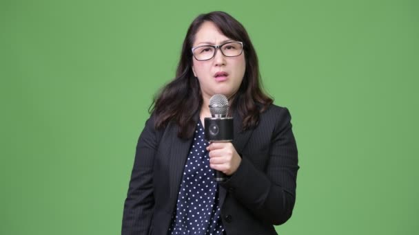 Mature sad Asian businesswoman as newscaster using microphone — Stock Video