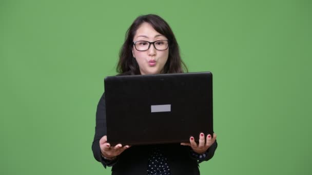 Mature beautiful Asian businesswoman using laptop against green background — Stock Video