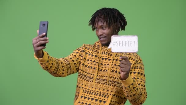 Joven hombre africano guapo tomando selfie con el cartel de papel — Vídeos de Stock