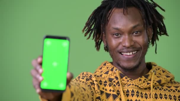 Молодой счастливый красивый африканский мужчина улыбается, показывая телефон — стоковое видео