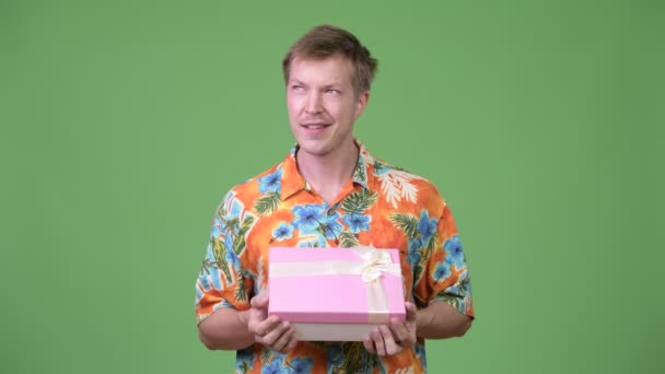Joven guapo turista sosteniendo caja de regalo y pensando — Vídeo de stock