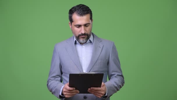 Красивий Перської бородатий бізнесмен, думаючи, утримуючи буфер обміну — стокове відео
