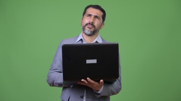 Handsome Persian bearded businessman thinking while using laptop — Stock Video