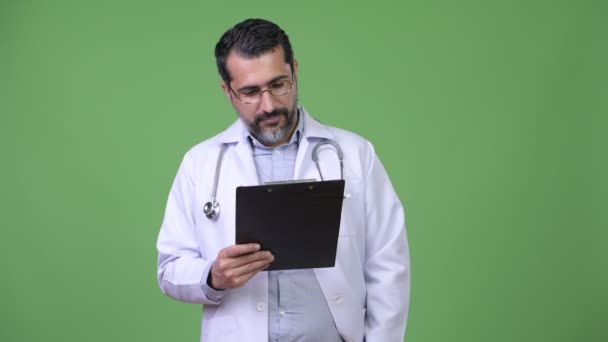 Handsome Persian bearded man doctor thinking while holding clipboard — Stock Video