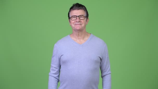 Happy hezký starší muž s úsměvem s brýlemi proti zeleným pozadím — Stock video