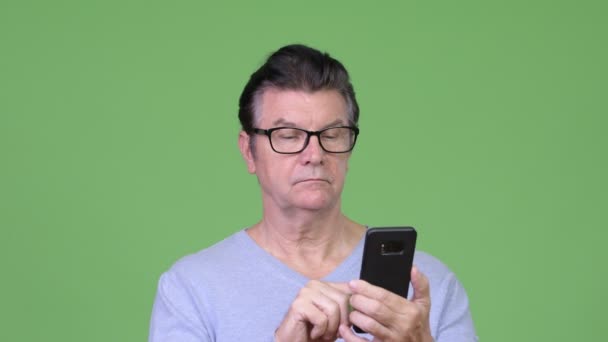Senior knappe man met behulp van telefoon en kijken verbaasd — Stockvideo