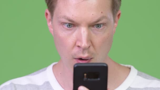 Młody przystojny mężczyzna przy użyciu telefonu i patrząc w szoku — Wideo stockowe