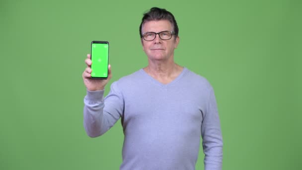 Senior knappe man tonen van de telefoon en geven duimen omhoog — Stockvideo