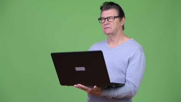 Senior gutaussehender Mann denkt während er Laptop benutzt — Stockvideo