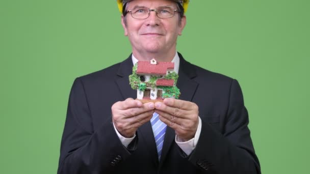 Старший привлекательный бизнесмен в качестве инженера, держащего фигурку дома — стоковое видео