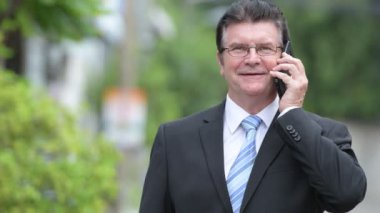 Açık havada sokaklarda telefonda konuşurken mutlu yakışıklı üst düzey iş adamı