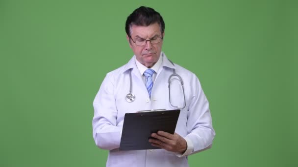 Senior handsome man doctor consulting while writing on clipboard — Stock Video