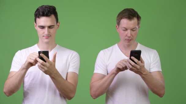 Twee gelukkige jonge knappe mannen samen gebruiken van telefoons — Stockvideo