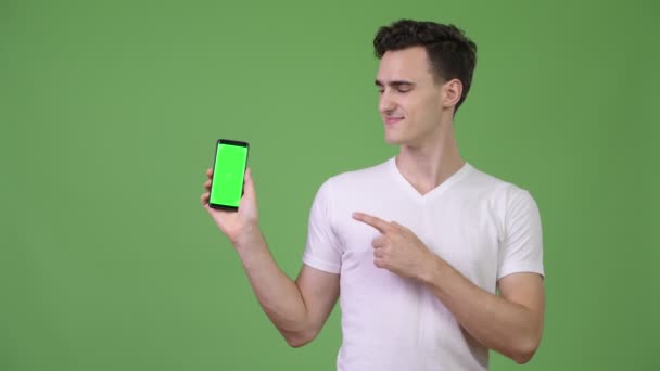 Young handsome man showing phone and giving thumbs up — Stock Video