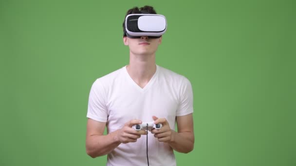 Молодой красивый мужчина играет в игры, используя гарнитуру виртуальной реальности — стоковое видео