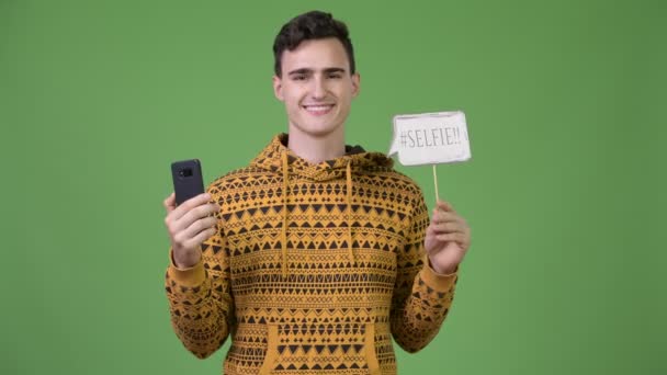 Mladý pohledný muž drží telefon a selfie papíru znamení — Stock video