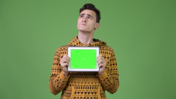 Joven hombre guapo pensando mientras muestra tableta digital — Vídeos de Stock