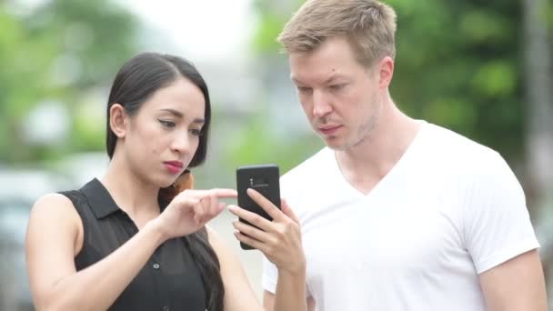 Νεαρό ζευγάρι πολυεθνικό χρησιμοποιώντας τηλέφωνο μαζί στους δρόμους σε εξωτερικούς χώρους — Αρχείο Βίντεο