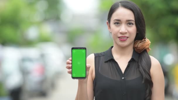 Joven feliz hermosa mujer de negocios asiática mostrando el teléfono en las calles al aire libre — Vídeos de Stock