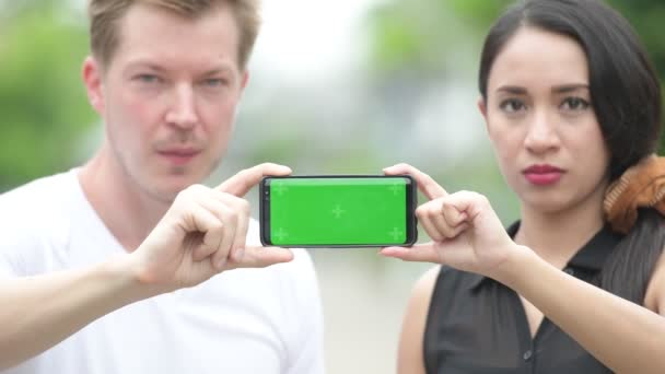 Jeune couple multi-ethnique montrant le téléphone ensemble dans les rues à l'extérieur — Video